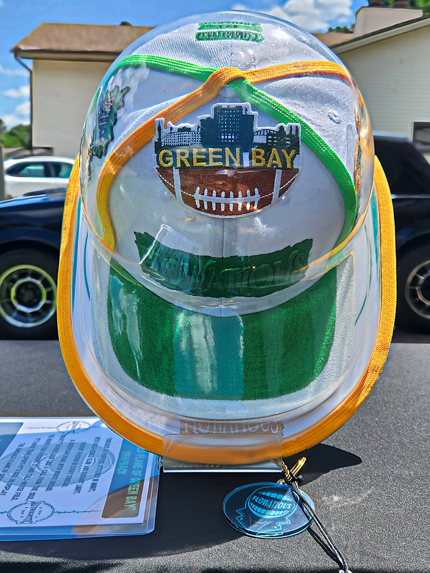 Clear protective case with custom snapback with 'Green Bay' branding on a stand outdoors.